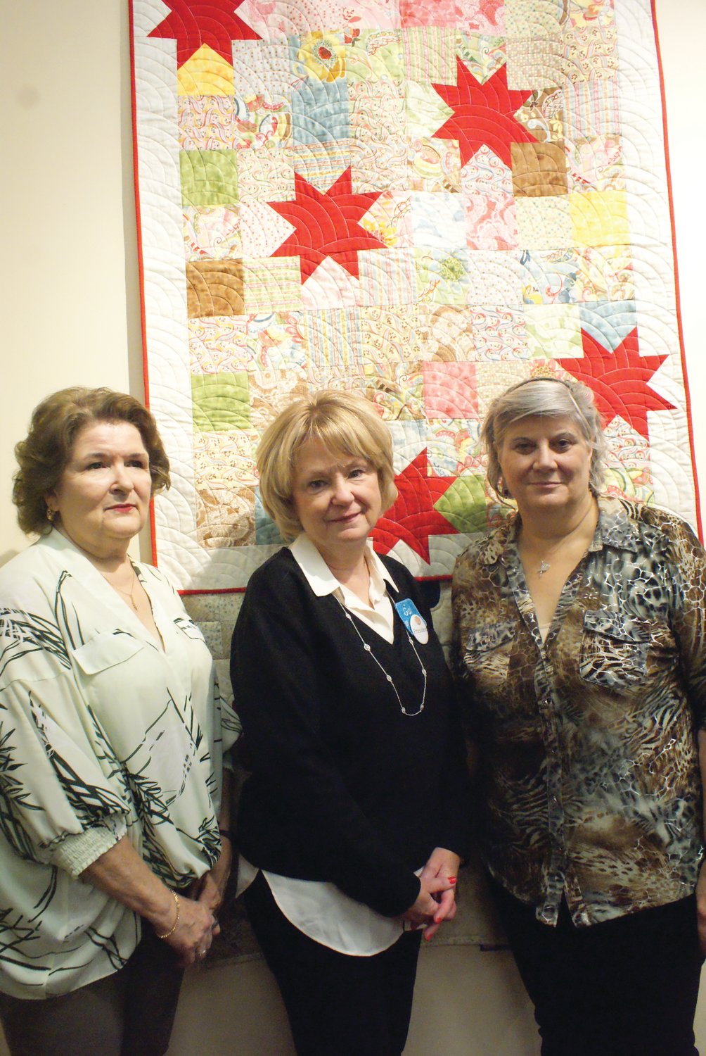 FABRIC CHALLENGE: Members of the Narragansett Bay Quilters’ Association (NBQA) pose with the quilt produced by the event’s co-chairwoman Barbara Hartford (left). In the middle is NBQA’s current president Gail Macera and on the far right is co-chairwoman Geri Bergreen.